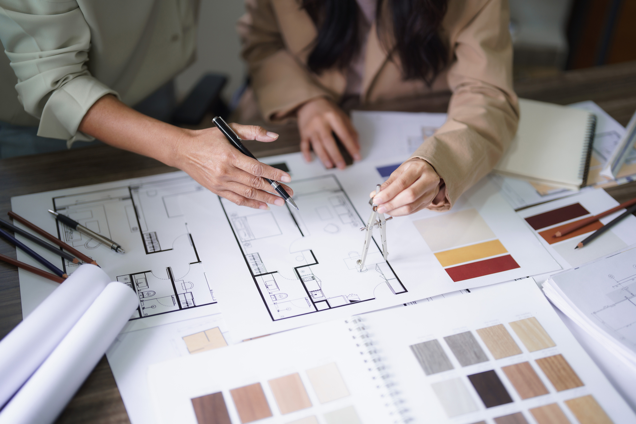 Two female architects discuss interior design building project and use divider compass on blueprint